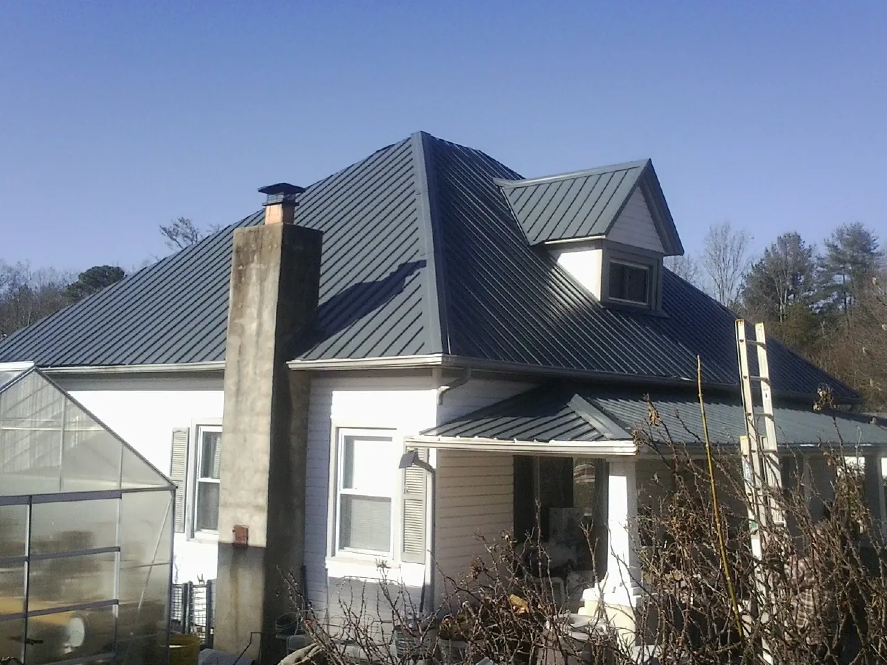 Dark blue standing seam metal roof on a white farmhouse with dormer — Slate & Tile Roof Repair by Roofing Brothers in Cuddy