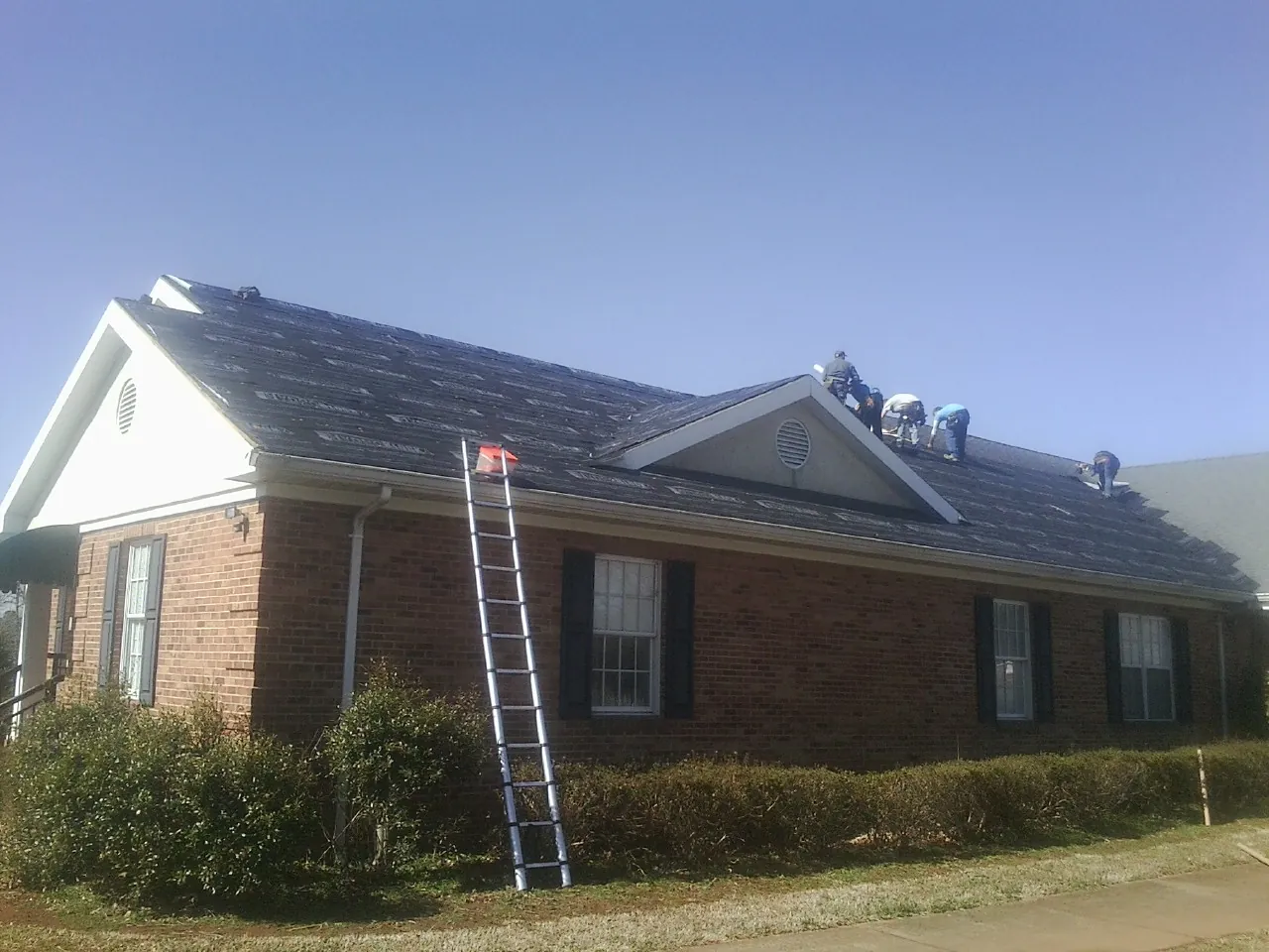 Crew tearing shingles off a brick ranch roof with a ladder set — Emergency Roof Repair work by our crew in Cuddy