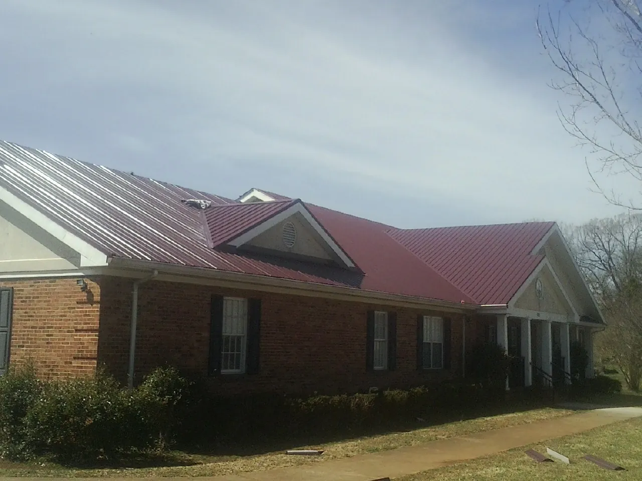 Red metal roof with gabled entries on a long brick building, from a Hail Damage Roof Repair job in Cuddy