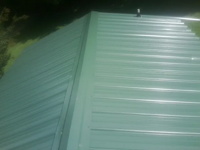 New green metal panels meeting at the ridge of a roof — Flat Roof Repair work by our crew in Cuddy