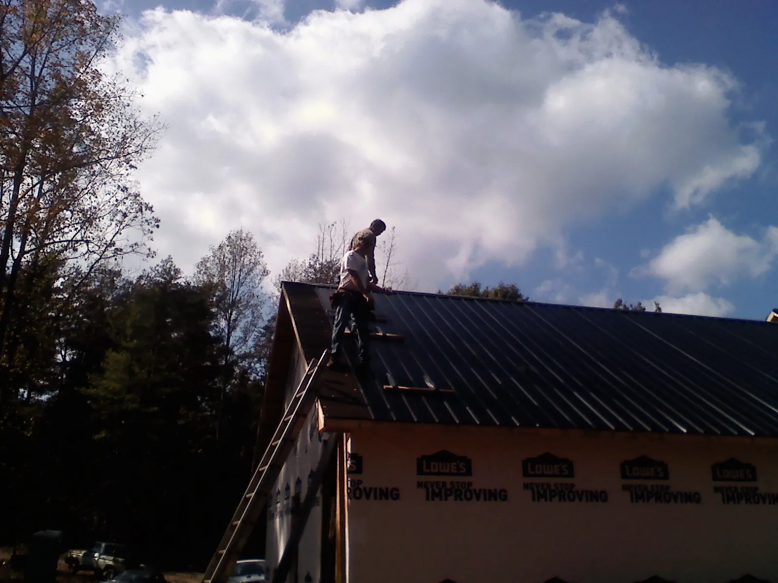 Roofer fastening dark metal panels high against a cloudy sky, from a Roof Inspection job in Cuddy