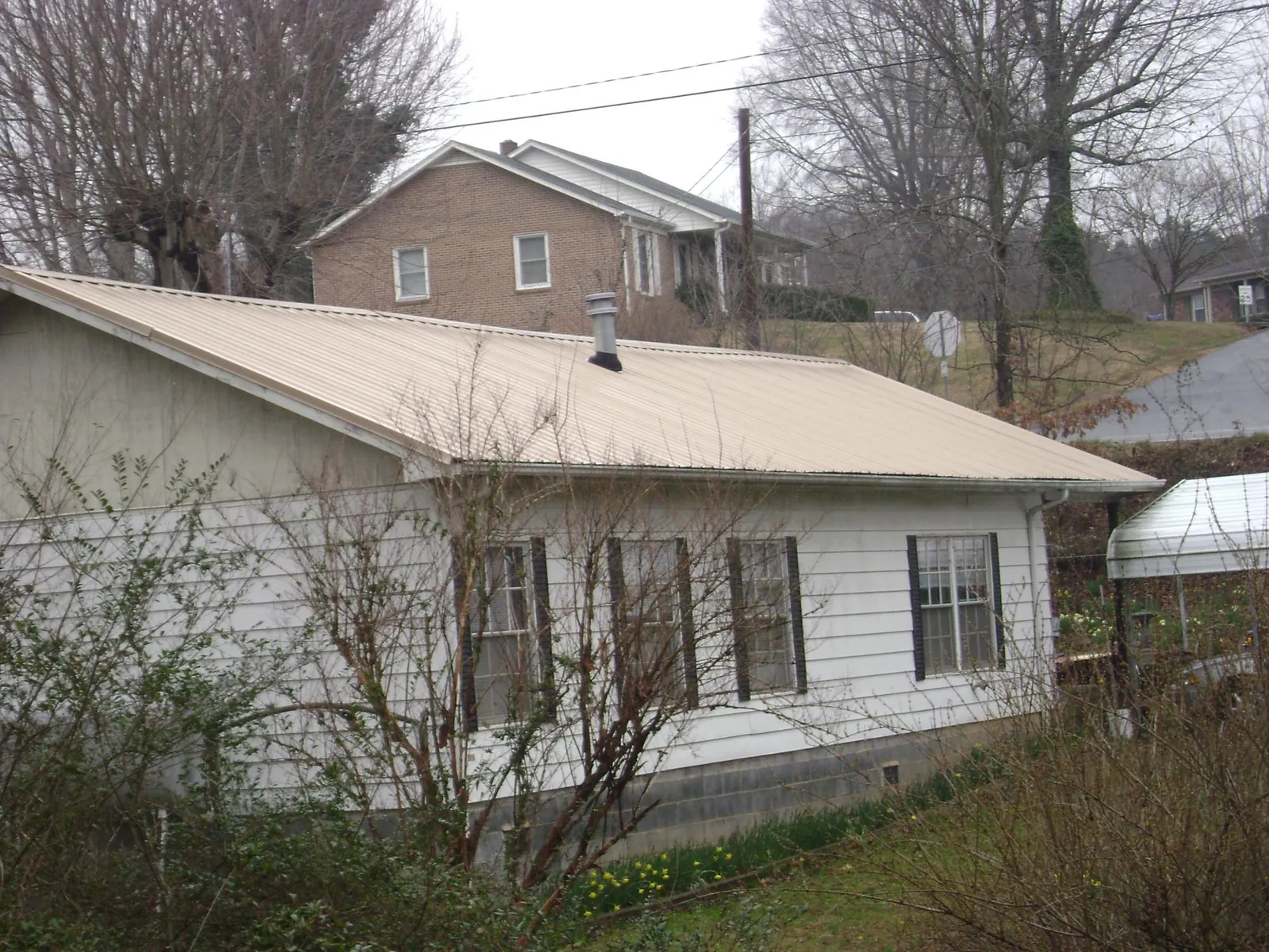 Tan metal roof on a white sided house set into a hillside — Commercial Roofing by Roofing Brothers in Cuddy